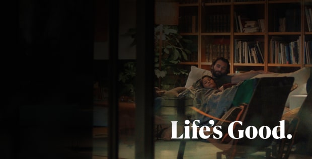 Một người đàn ông đang ngồi trên ghế sofa trước một kệ sách. Một người phụ nữ đang tựa vào cánh tay của người đàn ông. Dòng chữ "Life's Good" được viết bên dưới hình ảnh.